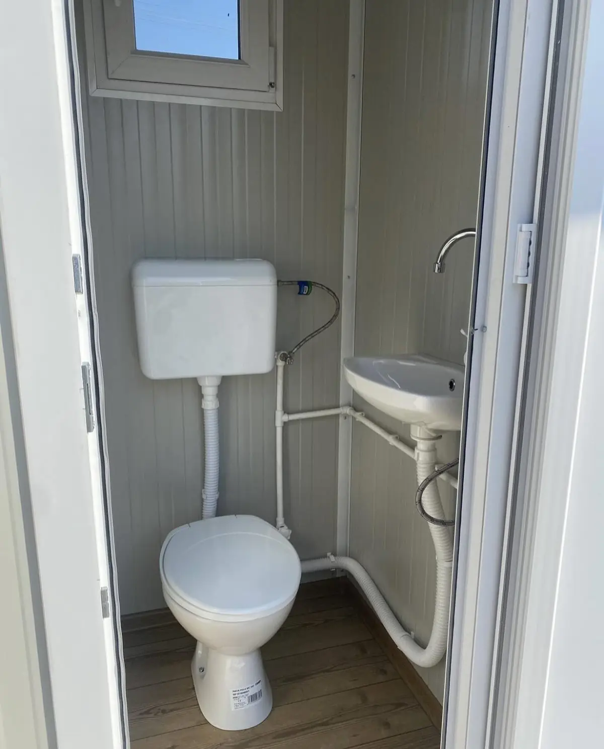 Flushing toilet and small sink inside a white restroom cabin