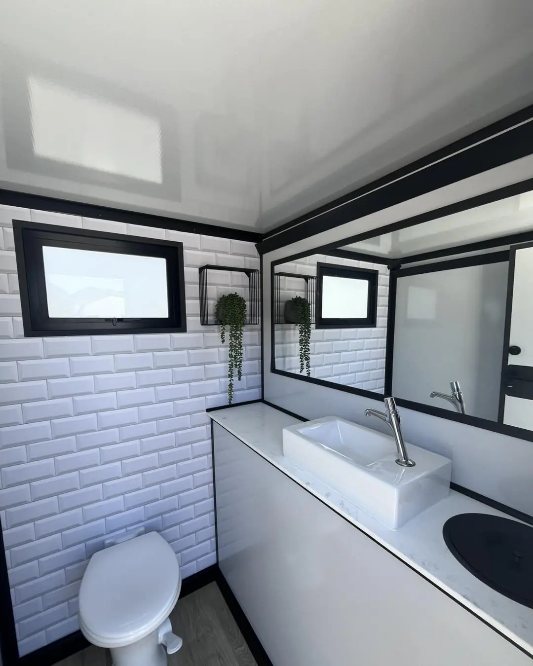 Restroom trailer stall with toilet, vanity sink and mirror