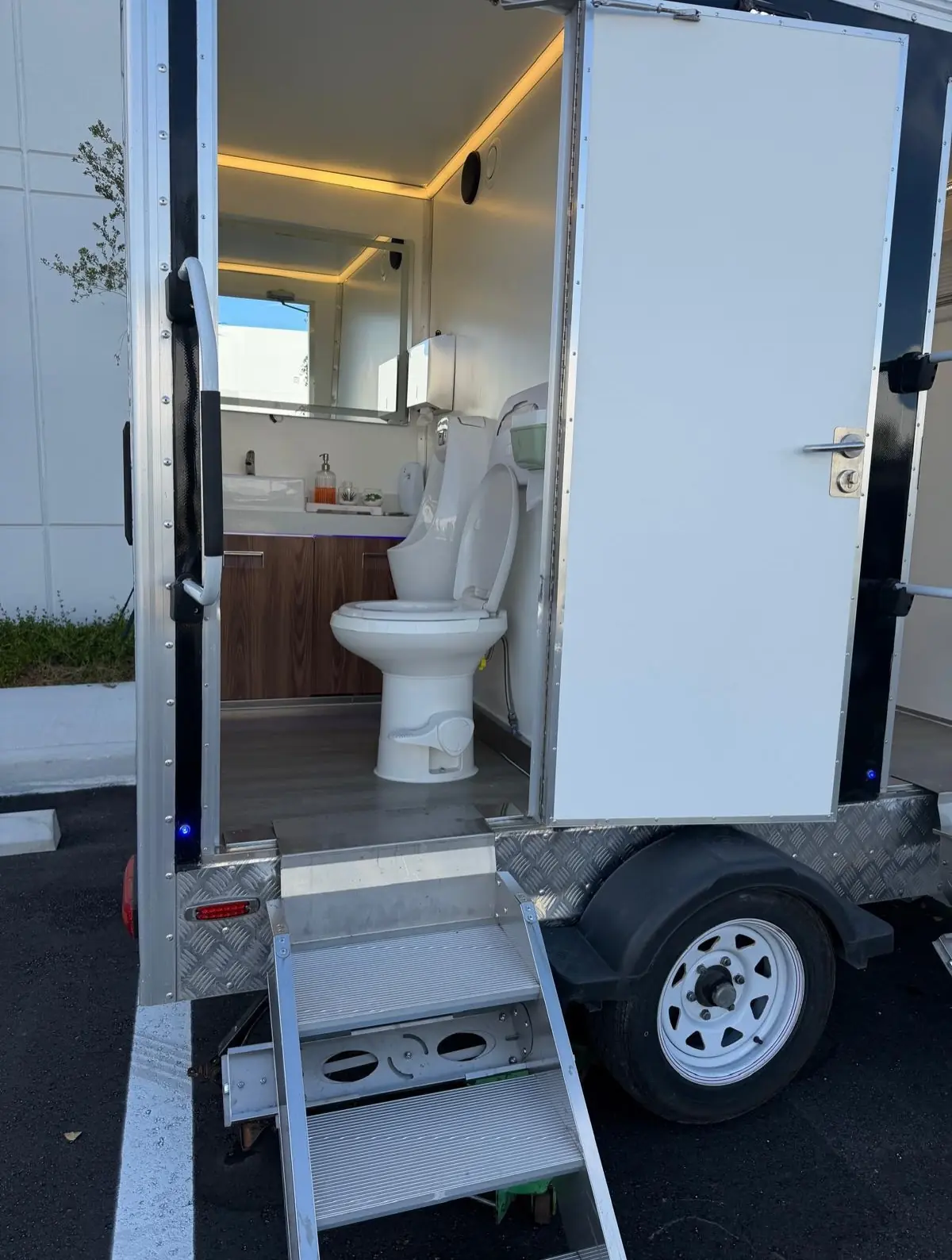 Open restroom trailer door showing steps, toilet and lighting
