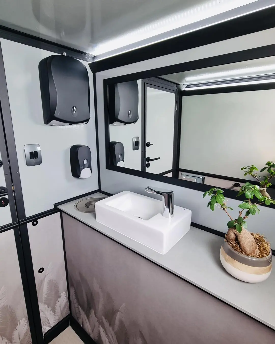 Restroom trailer vanity with a white sink, faucet and mirror