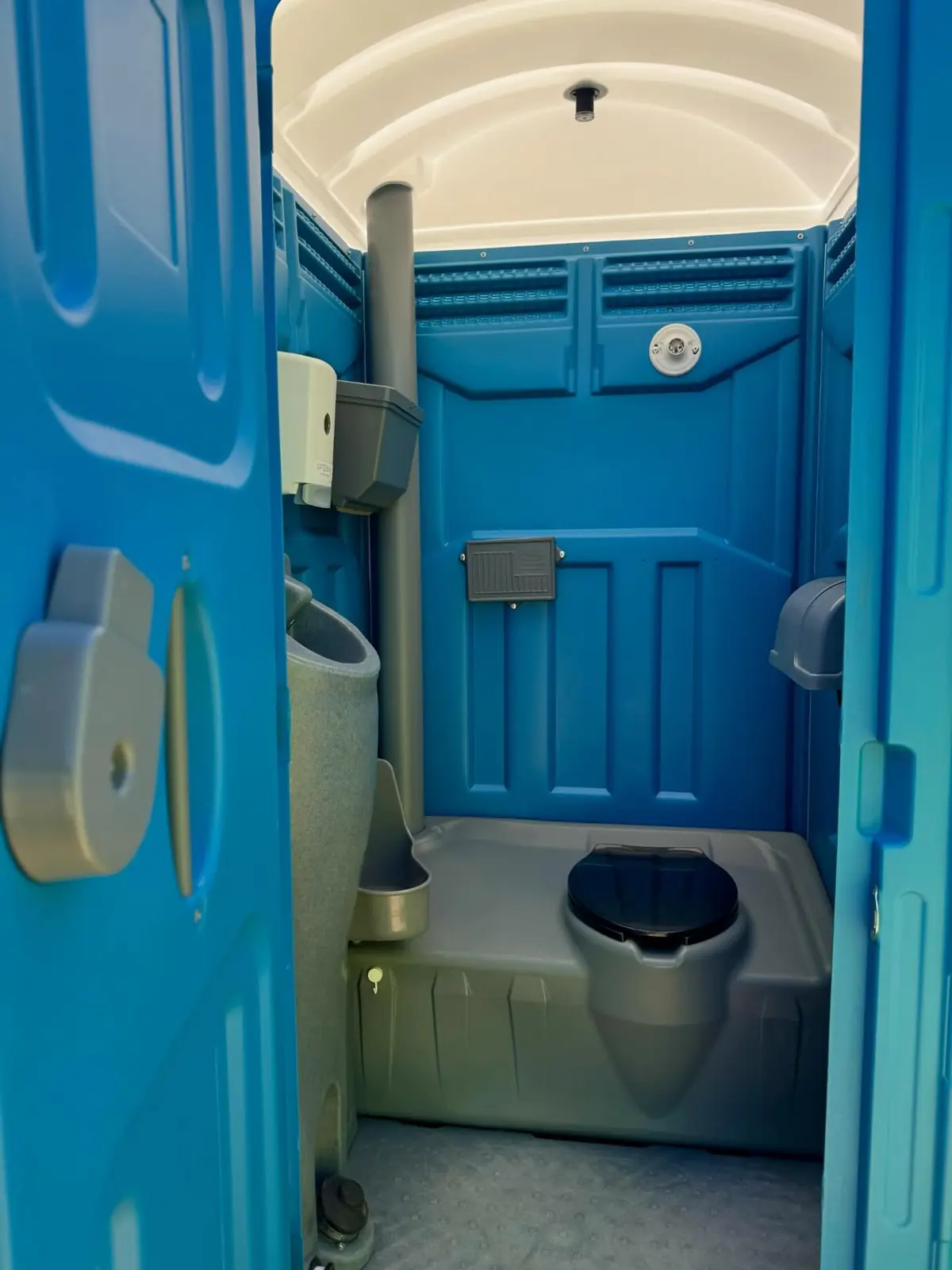 Inside a standard porta potty showing the toilet seat, urinal and paper holder